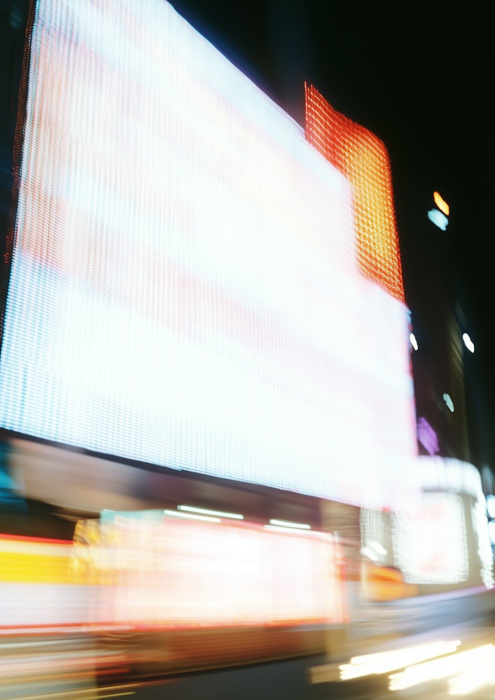 Blurred night street with glowing white and orange billboards and streaks of passing light